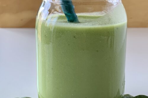 Green smoothie in a glass jar surrounded by baby spinach leaves