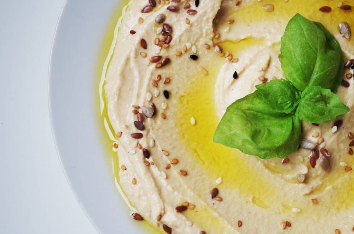 Closeup of Hummus topped with olive oil, sesame seeds and basil leaves