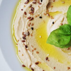 Closeup of Hummus topped with olive oil, sesame seeds and basil leaves