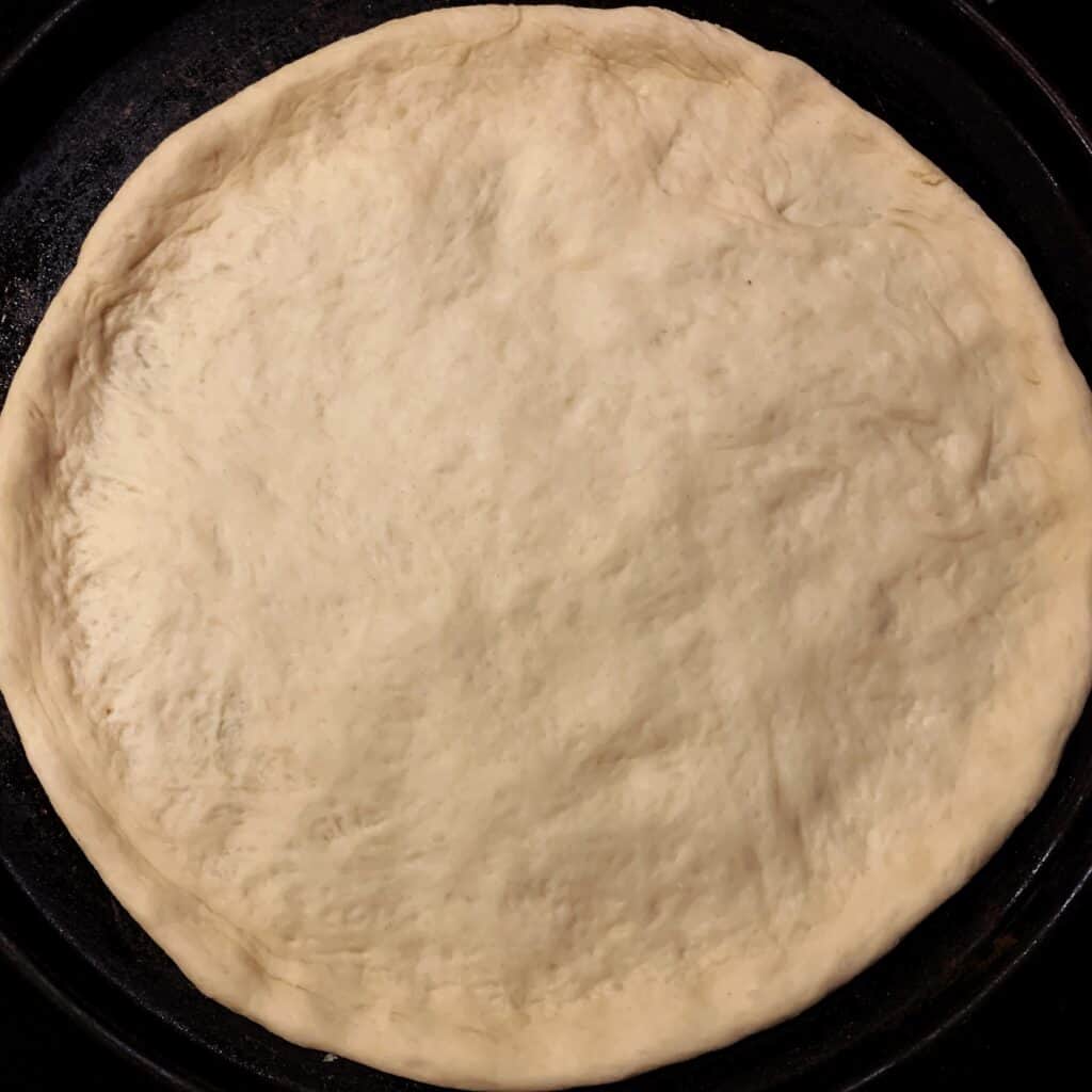 Raw pizza dough pressed into pizza pan
