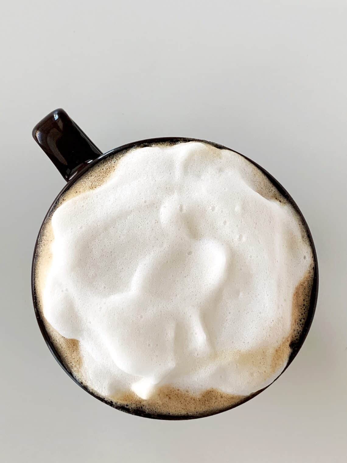 Overhead view of almond milk latte made with brown sugar syrup, topped with almond milk foam in a brown mug