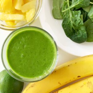 Pineapple lime green smoothie in a glass with fresh pineapple, spinach, bananas, and lime.