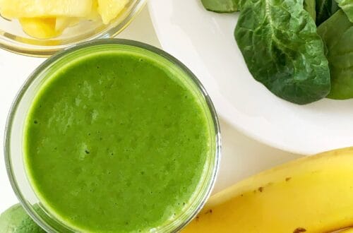 Pineapple lime green smoothie in a glass with fresh pineapple, spinach, bananas, and lime.