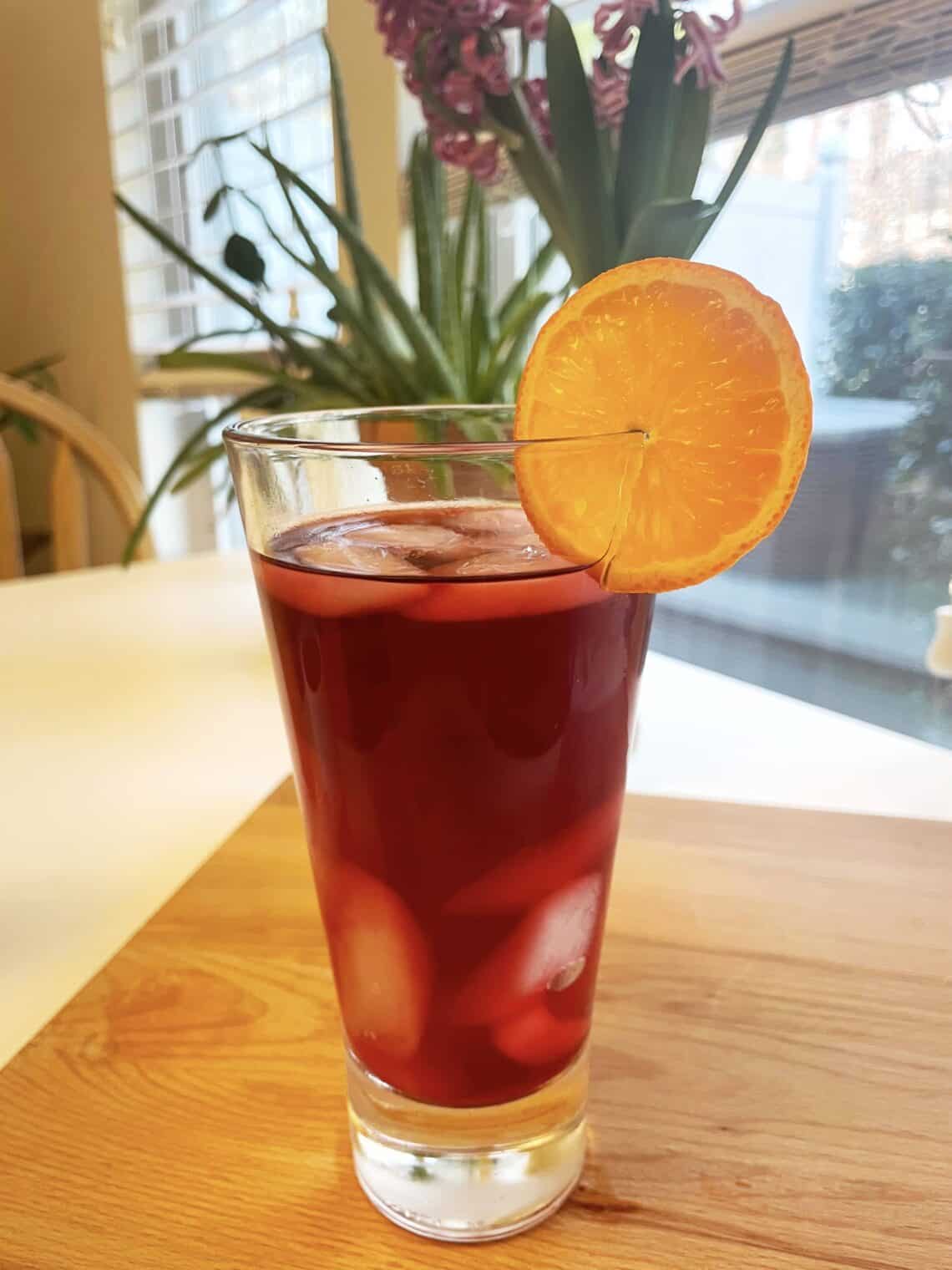 Glass of Iced Mandarin Hibiscus Tea garnished with an orange slice