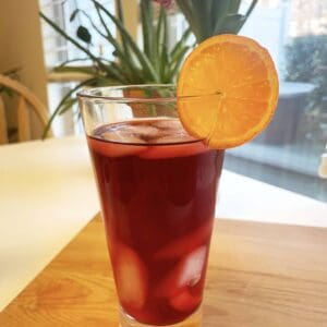 Glass of Iced Mandarin Hibiscus Tea garnished with an orange slice