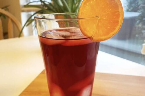 Glass of Iced Mandarin Hibiscus Tea garnished with an orange slice