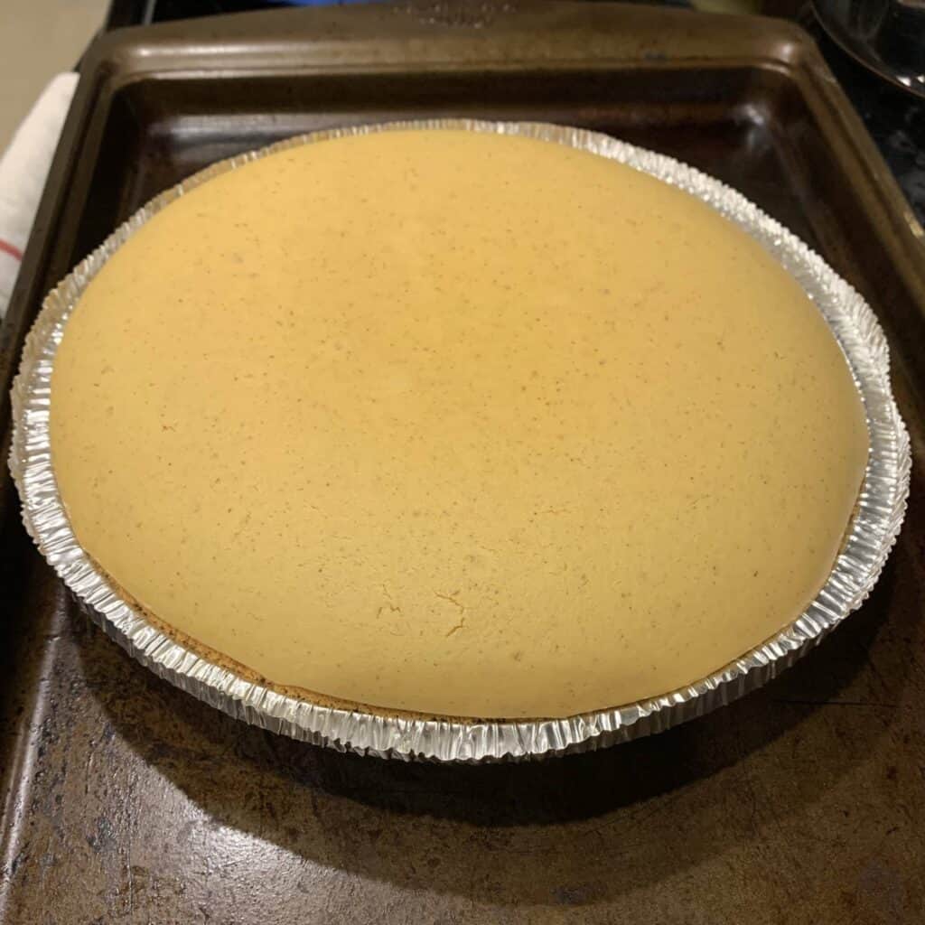 Close-up of baked pumpkin cheesecake with graham cracker crust on a baking sheet.