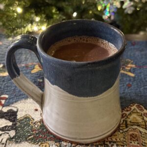 Mug of spiked butterscotch hot chocolate in front of Christmas tree in the background