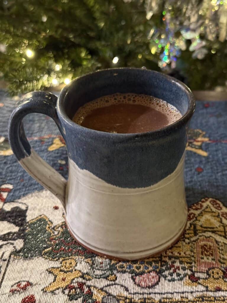 Mug of spiked butterscotch hot chocolate in front of Christmas tree in the background