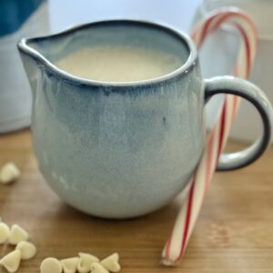 White Chocolate Peppermint Creamer in a blue ceramic creamer with white chocolate chips and peppermint candy cane