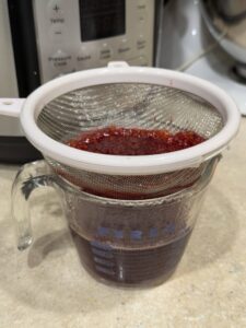 Straining raspberry vanilla syrup with a fine mesh sieve into a glass measuring cup.